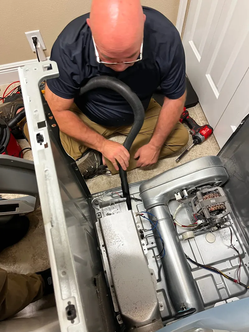 Technician vacuuming lint from an open dryer cabinet