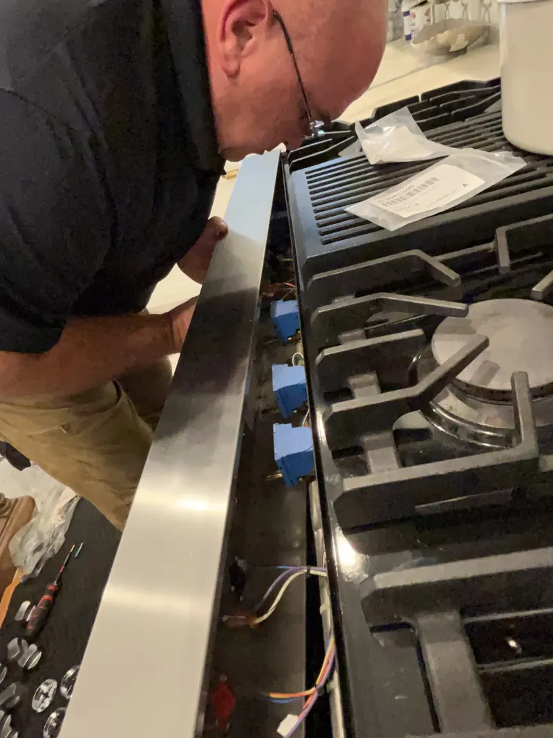 Technician repairing a gas cooktop burner assembly