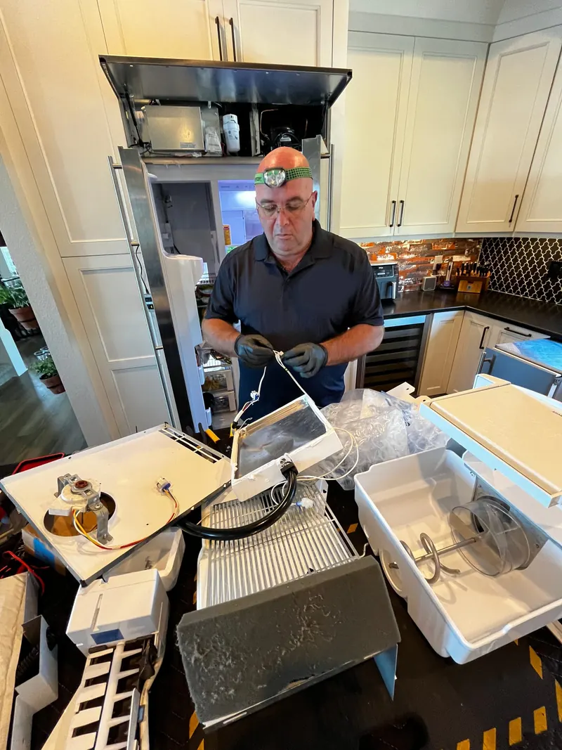 Technician rebuilding a refrigerator ice maker in a home kitchen