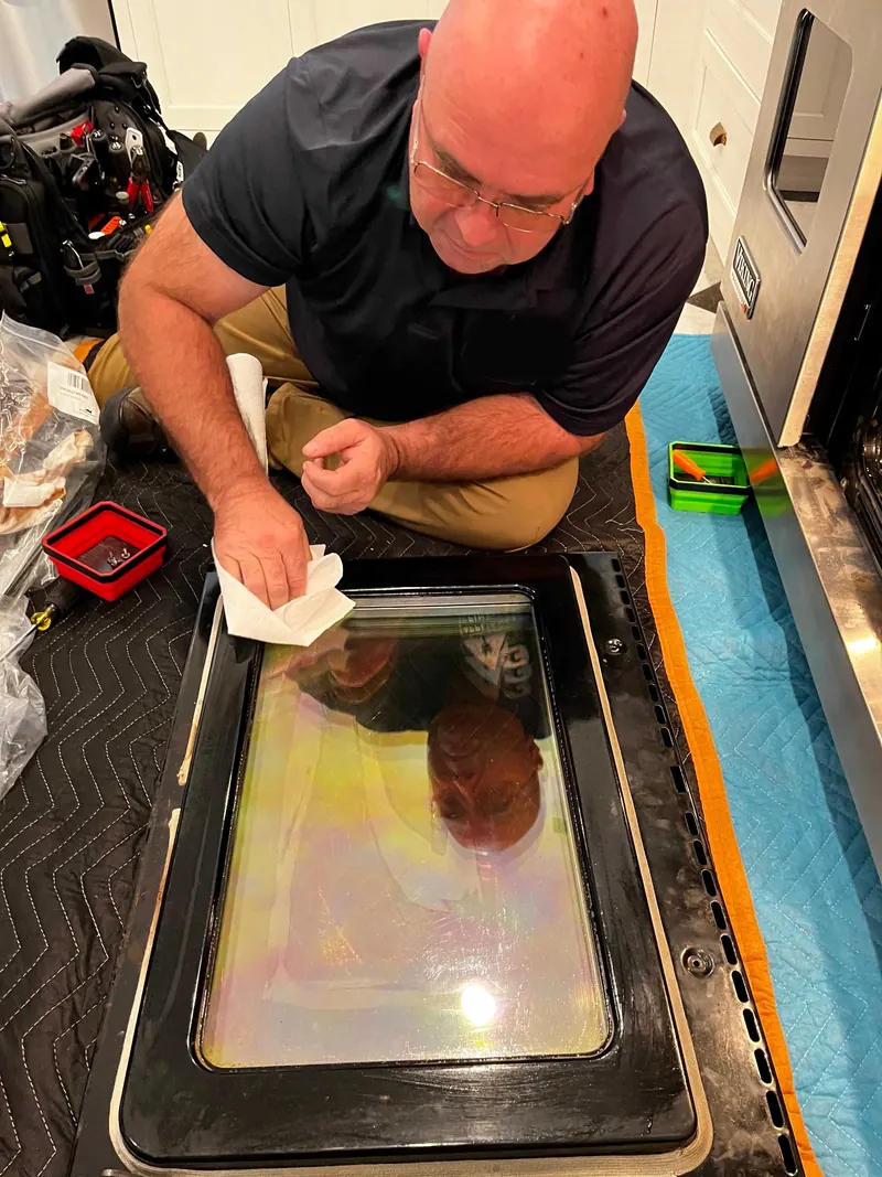 Technician cleaning an oven door glass panel